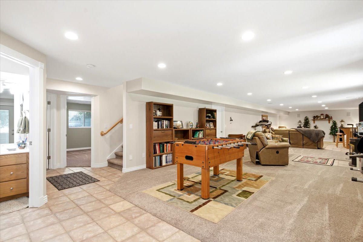 Expansive lower-level space featuring recessed lighting, a combination of tile and carpeted flooring, and a built-in staircase with wood railing
