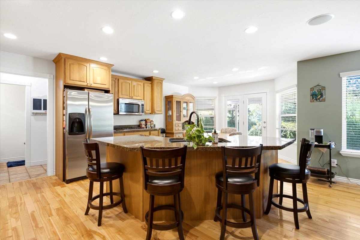Kitchen featuring a central island with a granite countertop, light wood cabinetry, stainless steel appliances, wood-finish flooring, and recessed ceiling lighting