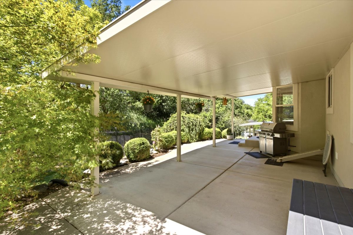Expansive covered patio featuring a concrete surface, multiple support columns, and lush surrounding landscaping