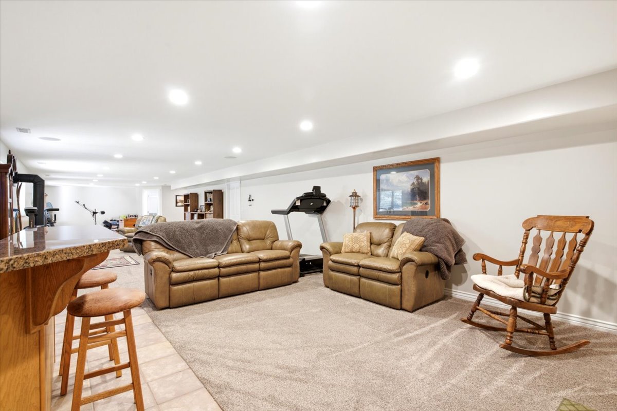 Spacious finished lower level featuring recessed lighting, a built-in bar with stone-finish countertop, tile flooring, and carpeted lounge area