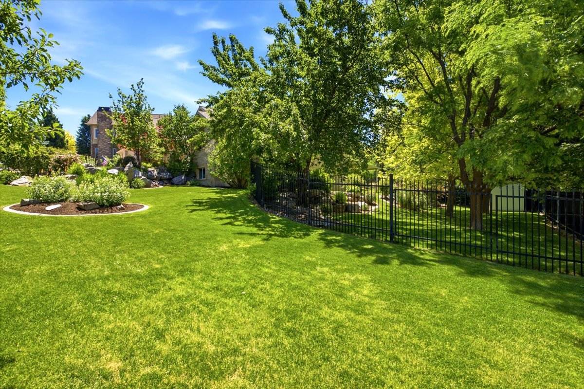 Expansive lawn area featuring a decorative rock garden, mature trees, and a black wrought iron fence