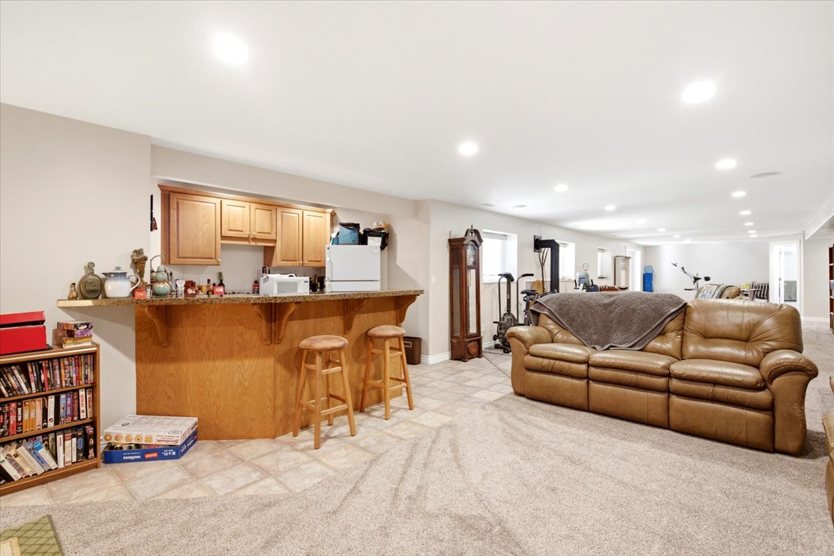 Spacious lower-level area featuring a built-in wet bar with wood-finish cabinetry, a stone-finish countertop, and wood-finish paneling