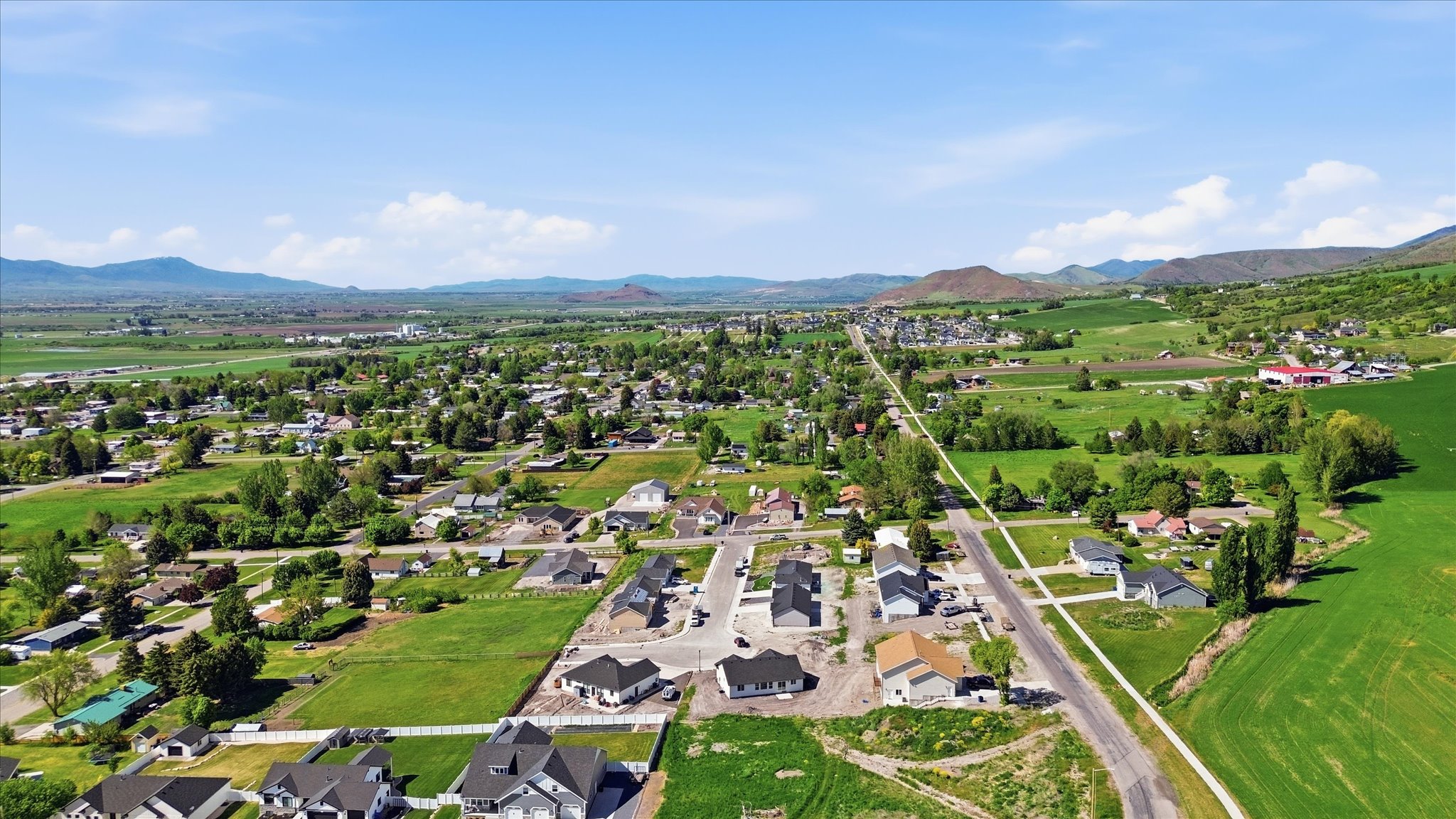 Rural community setting with expansive green fields, mature trees, and distant mountain ranges