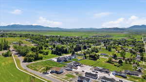Aerial depiction of a developing community with new construction homes, established residences, expansive green fields, mature trees, and distant mountains