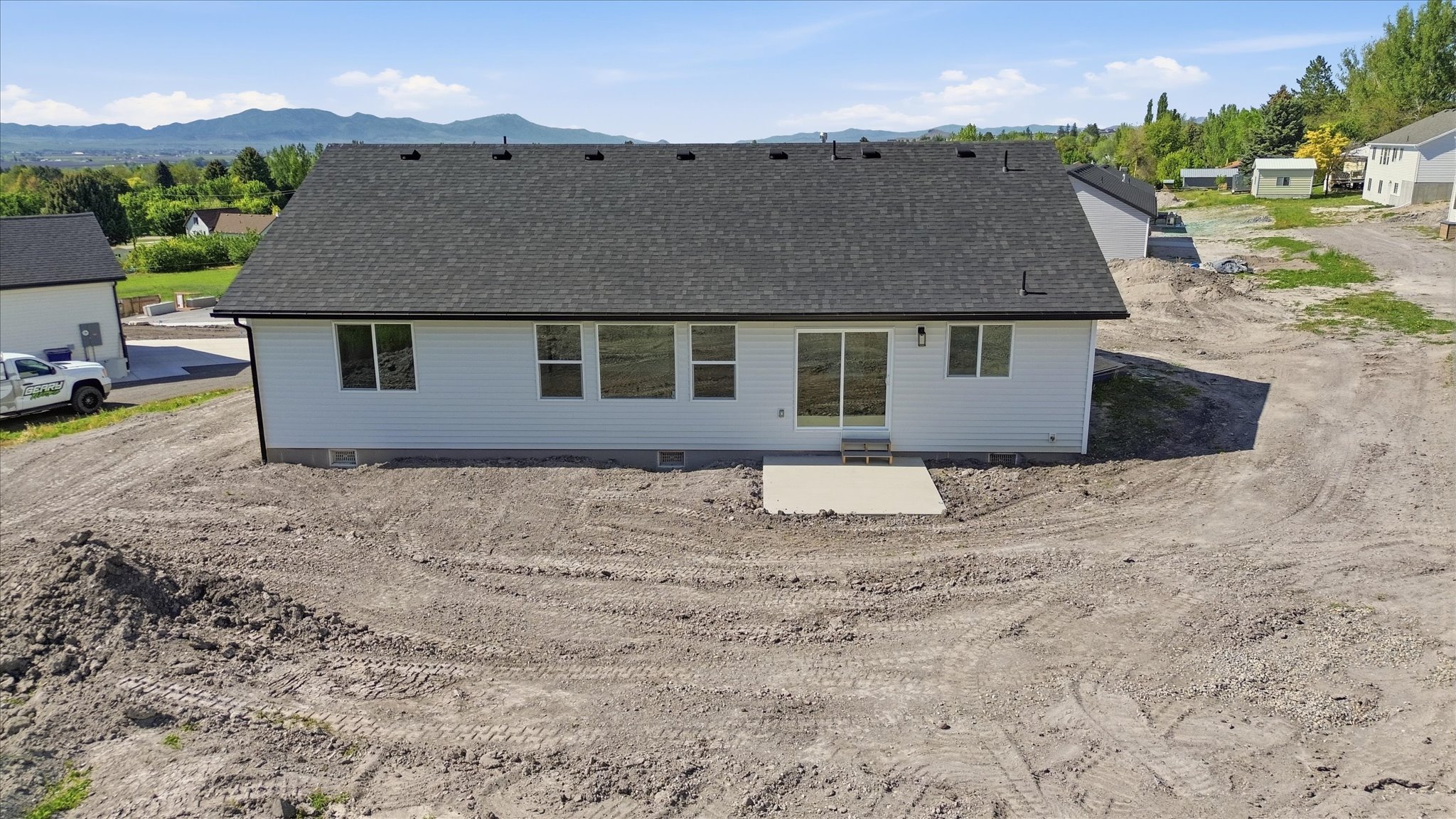 Newly constructed residence featuring white siding, a dark shingle roof, and a concrete patio
