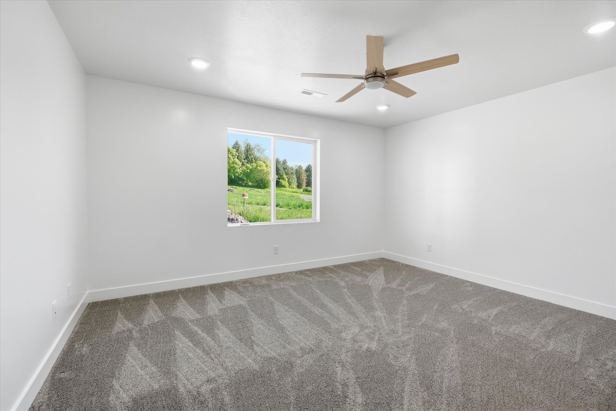 Spacious room featuring neutral carpeting, a large window, a wood-finish ceiling fan, recessed lighting, and white baseboards