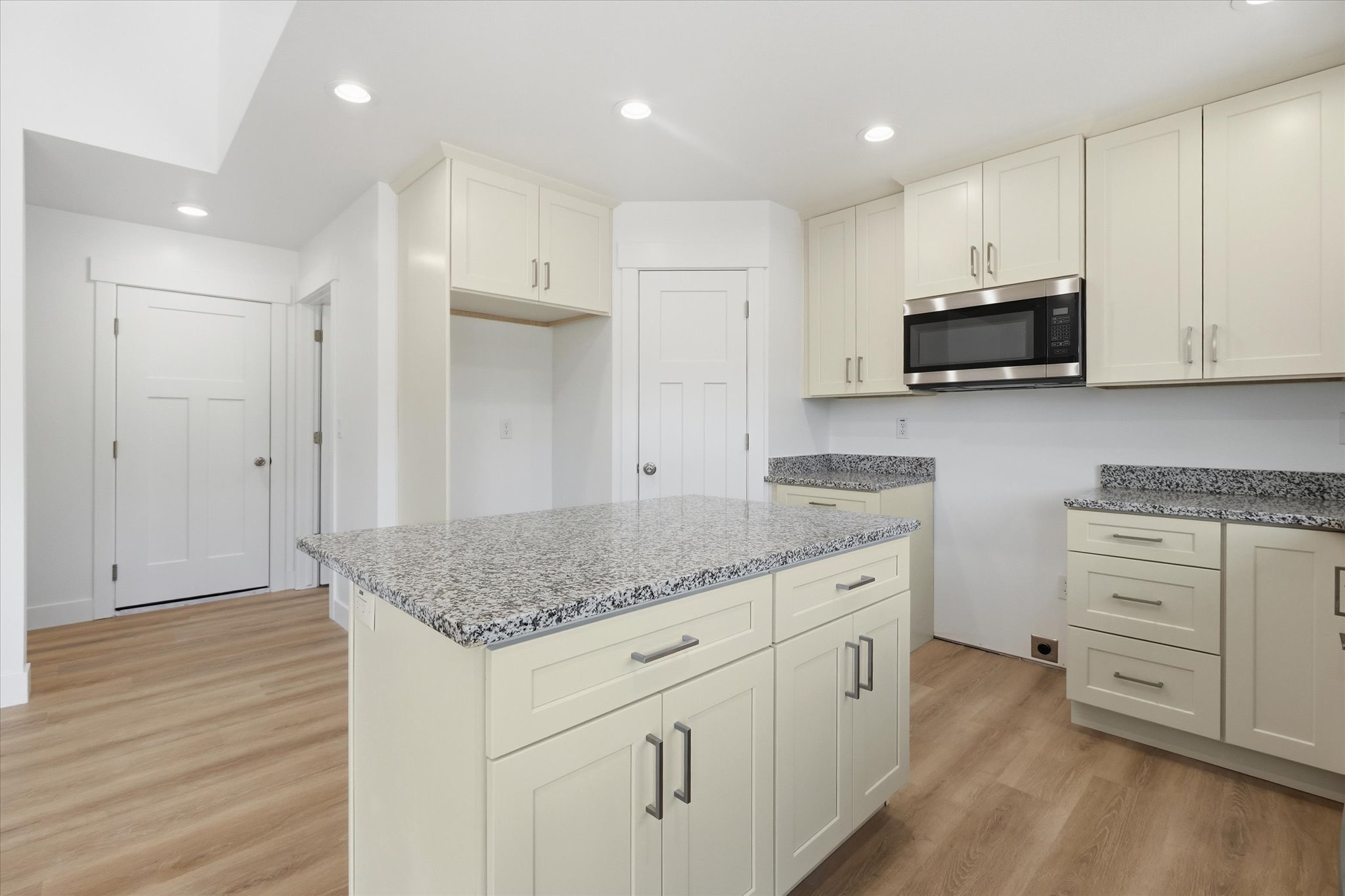 Modern kitchen featuring an island with a speckled countertop, extensive cabinetry, wood-finish flooring, recessed lighting, and a stainless steel microwave
