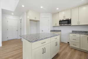 Modern kitchen featuring an island with a speckled countertop, extensive cabinetry, wood-finish flooring, recessed lighting, and a stainless steel microwave