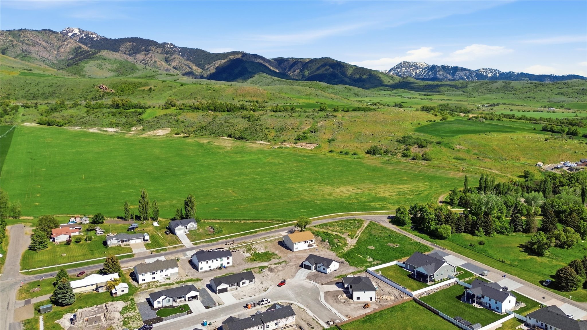 Expansive green fields bordering a developing residential area with mountain scenery