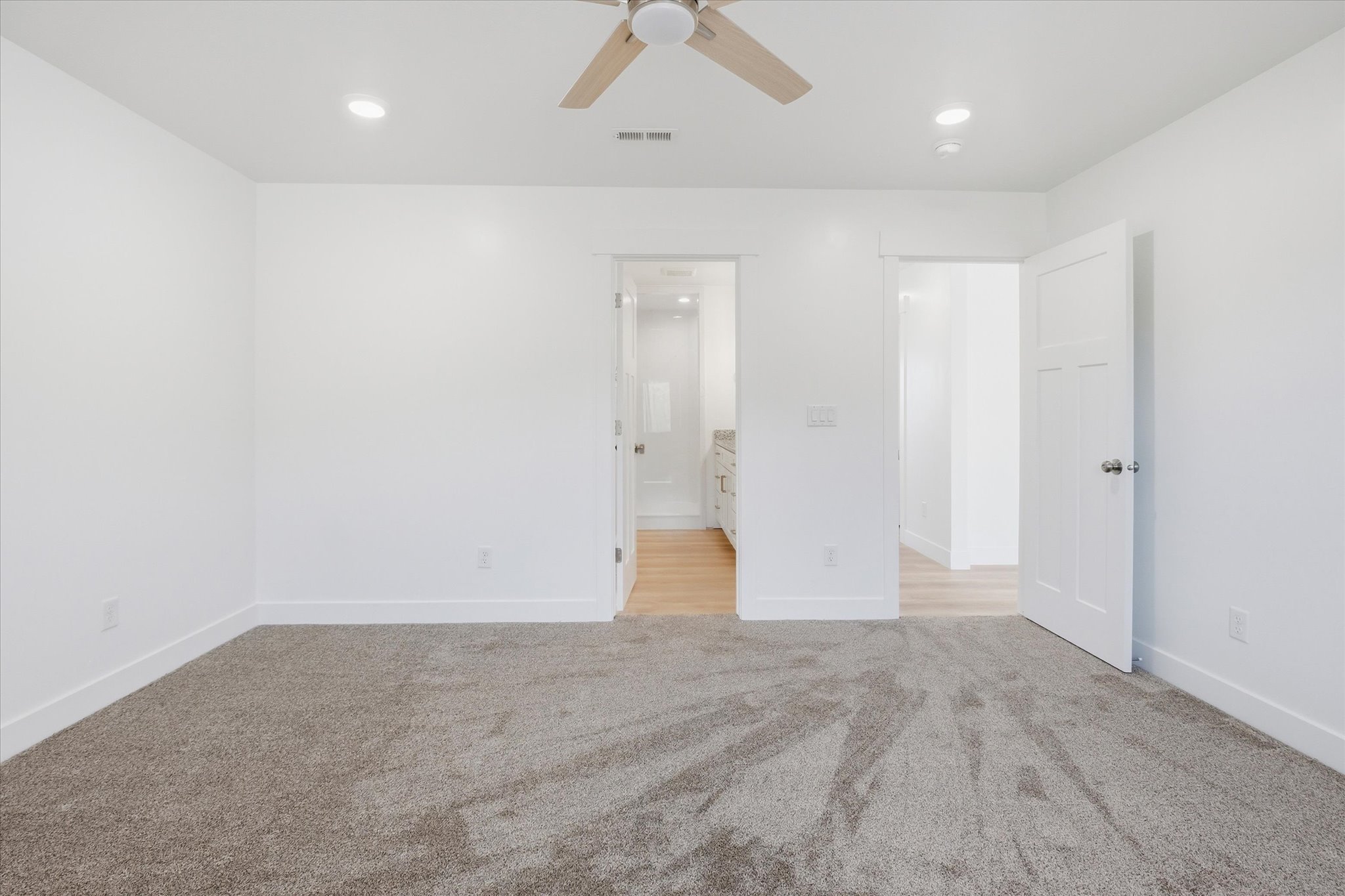 Spacious room featuring neutral carpeting, white walls, recessed lighting, and a ceiling fan with wood-finish blades