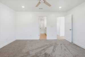 Spacious room featuring neutral carpeting, white walls, recessed lighting, and a ceiling fan with wood-finish blades