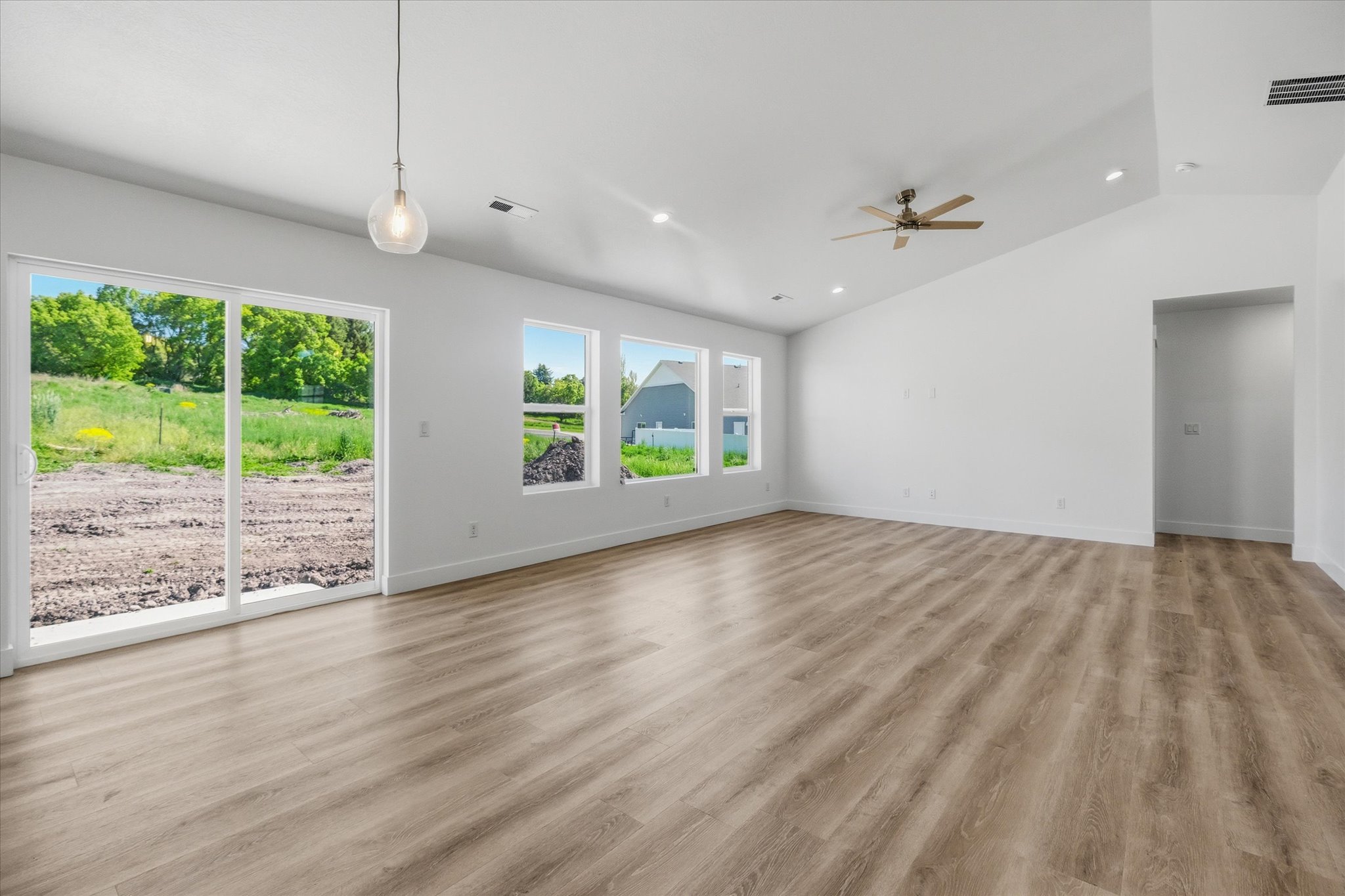Spacious room featuring wood-finish flooring, white walls, and a vaulted ceiling