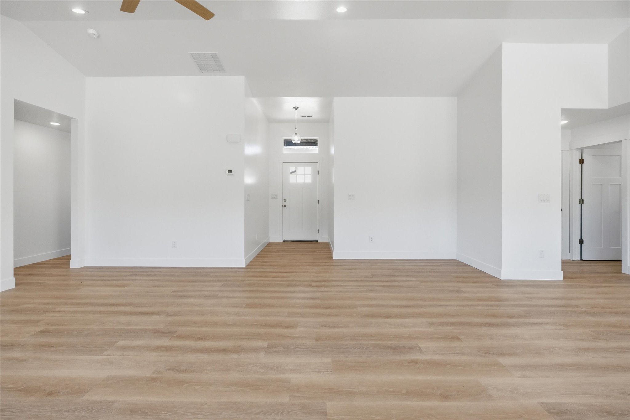 Expansive open-concept living space featuring wood-finish flooring, recessed lighting, and a neutral white color palette