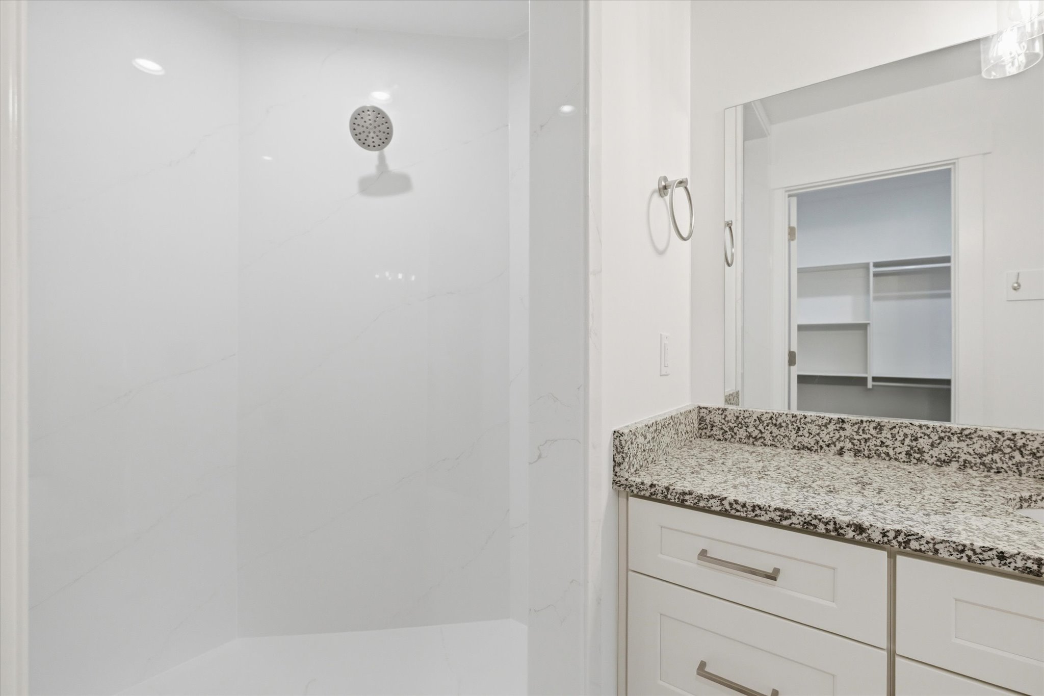 Shower with a rainfall showerhead and white surround, complemented by a vanity featuring a speckled countertop and white cabinetry with brushed nickel hardware