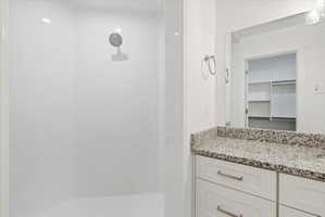 Shower with a rainfall showerhead and white surround, complemented by a vanity featuring a speckled countertop and white cabinetry with brushed nickel hardware