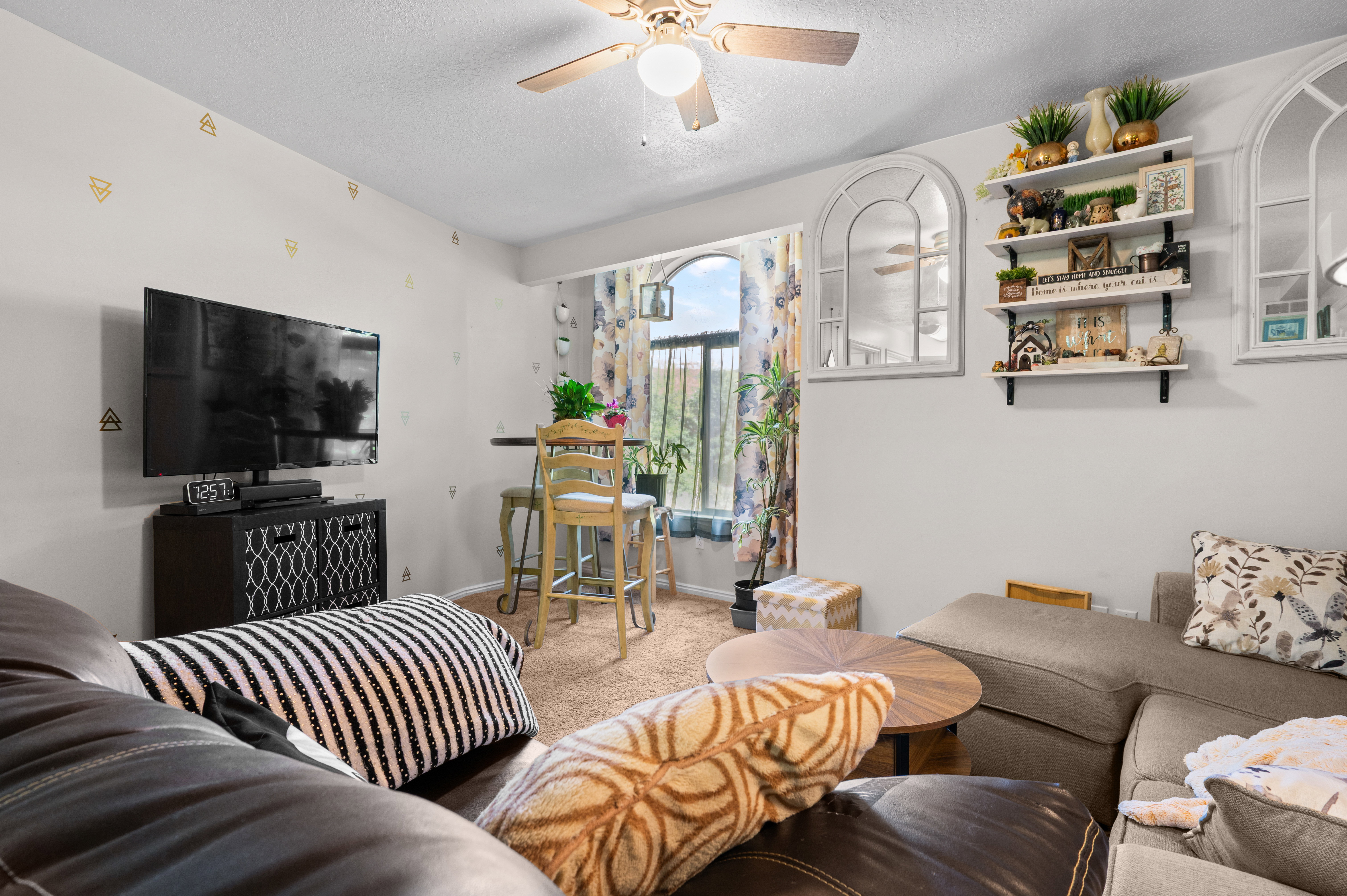 Living area featuring a ceiling fan, wall-mounted shelving, and arched decorative mirrors