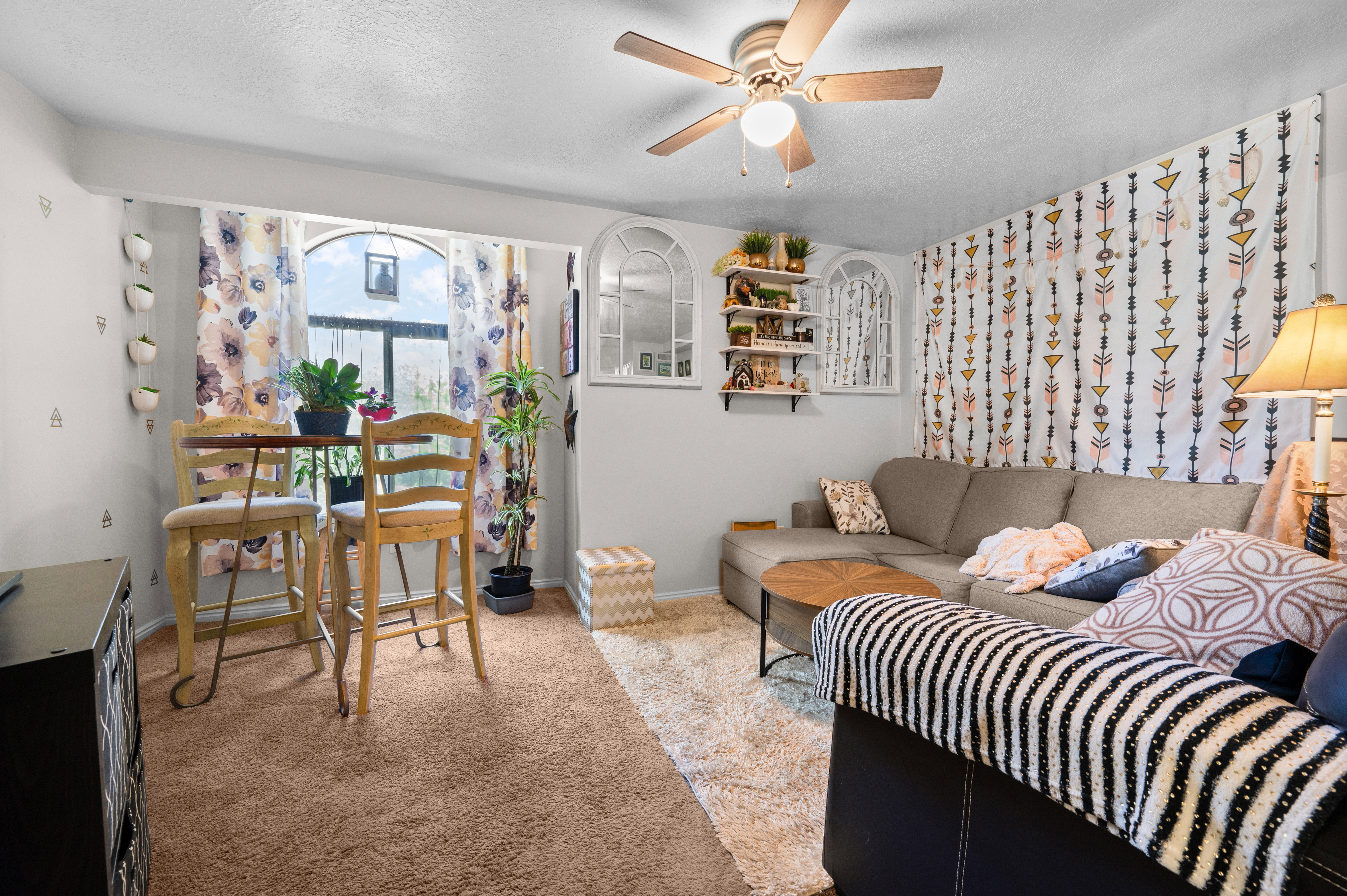 Living area featuring a ceiling fan, carpet flooring, and a large arched window with a deep sill