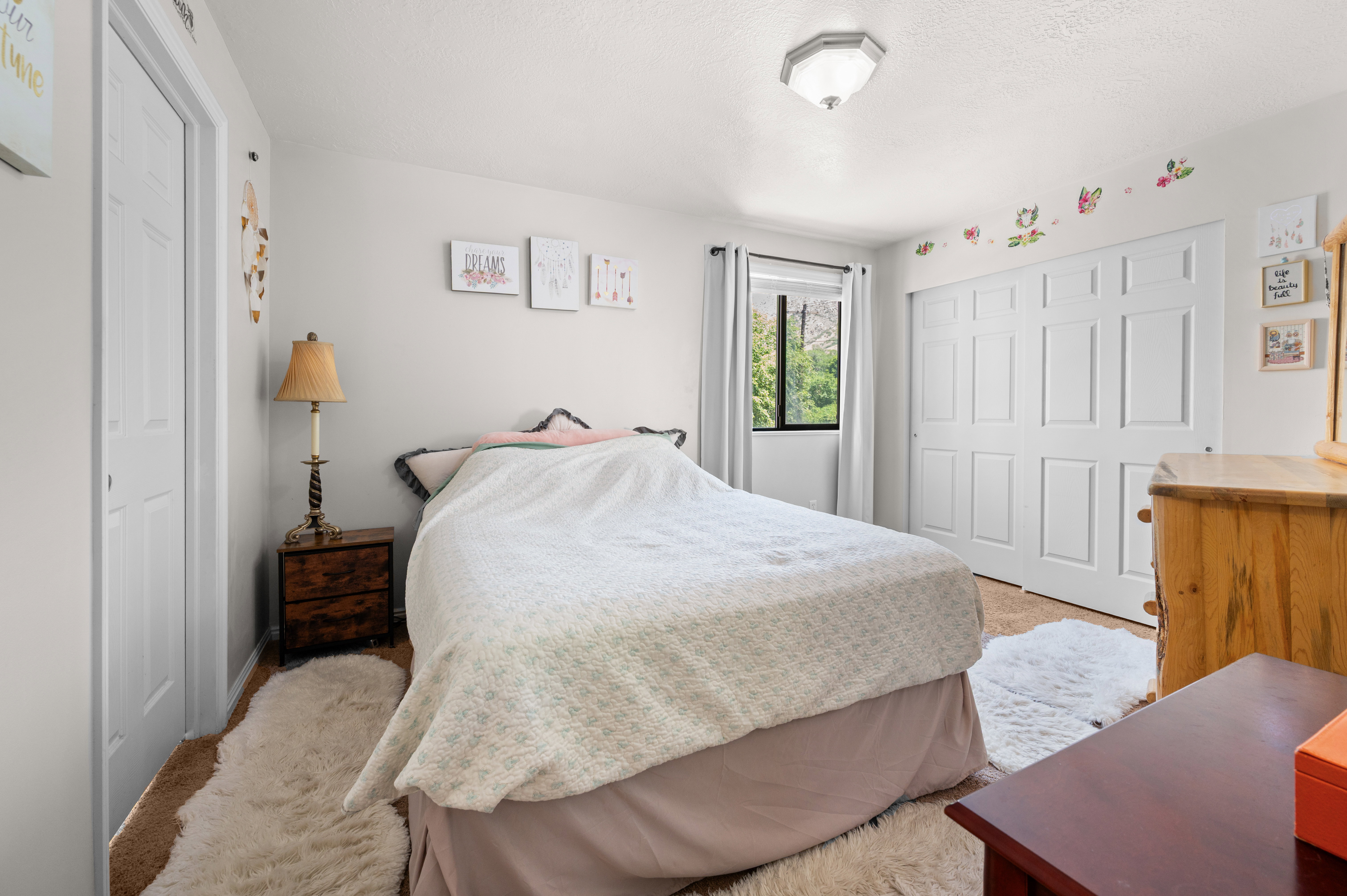 Bedroom featuring carpeted flooring, a ceiling-mounted light fixture, a window with white drapes, and white bi-fold closet doors