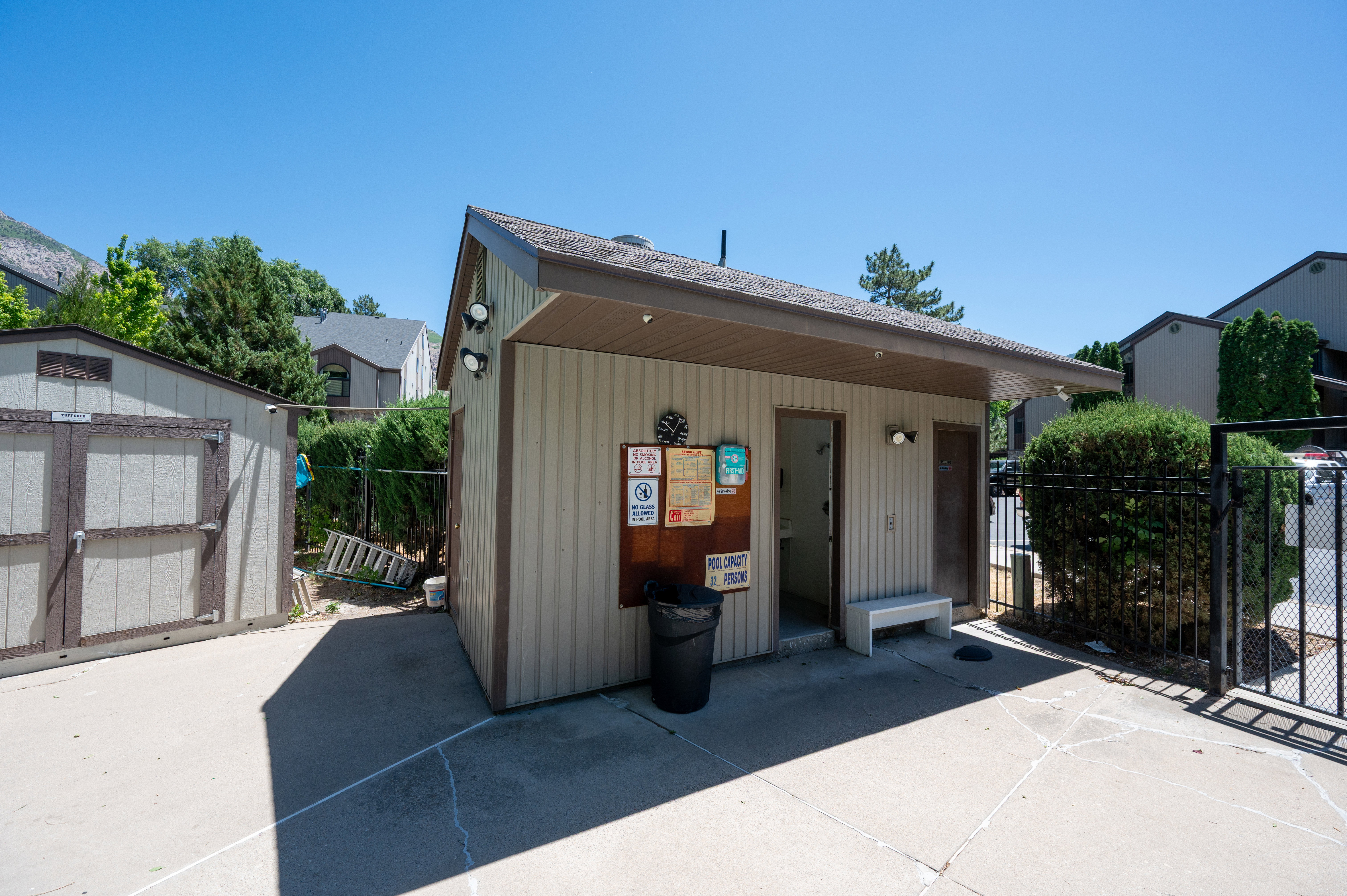 Pool house structure featuring vertical siding and a hip roof, accompanied by a utility shed with double doors