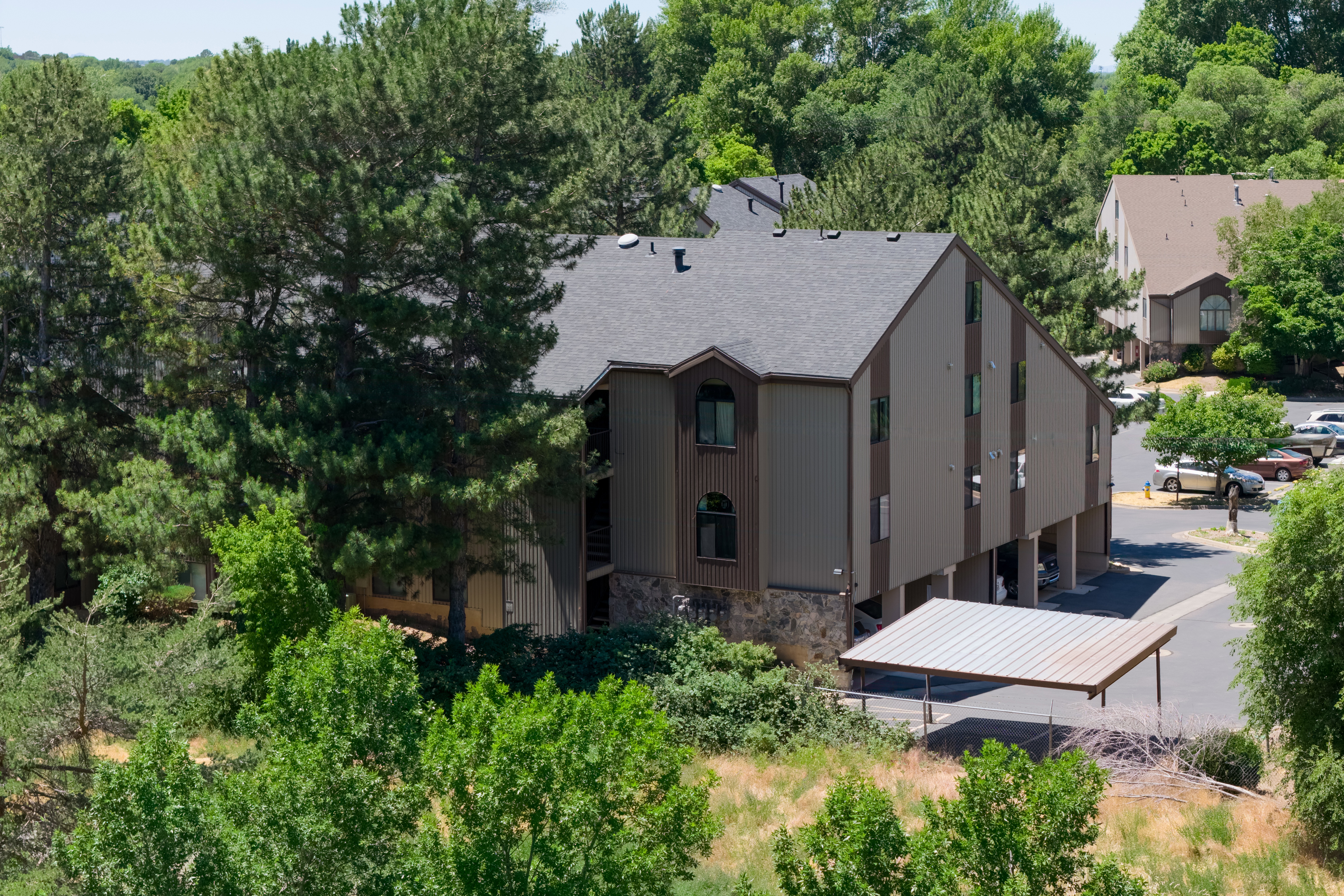 Multi-story residential building with a dark shingle roof, brown siding, stone foundation, and arched window details