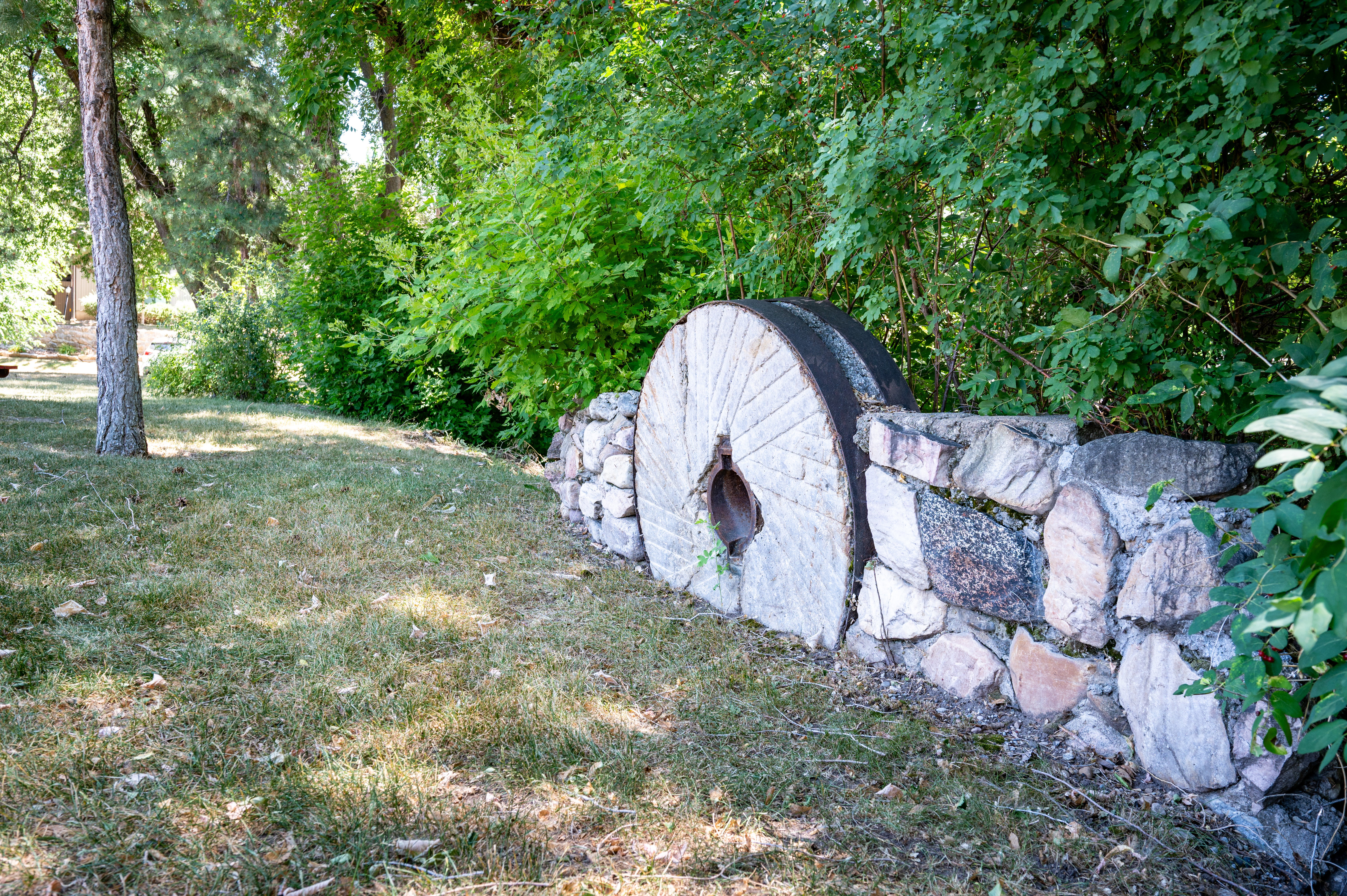Stone wall accent with integrated millstone, mature trees, and natural landscaping