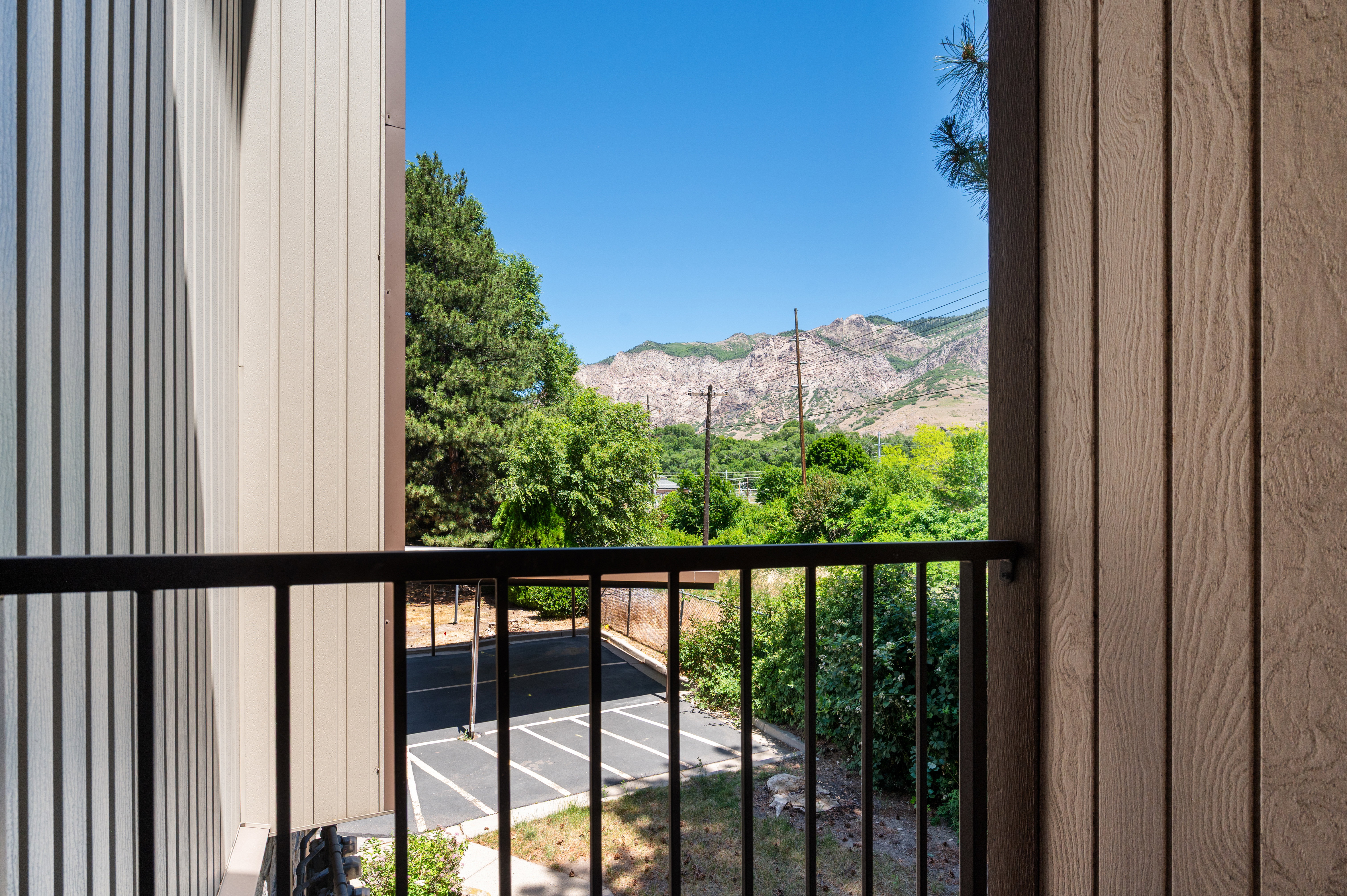 Exterior balcony with black metal railing, featuring a mountainous backdrop, expansive blue sky, and surrounding greenery