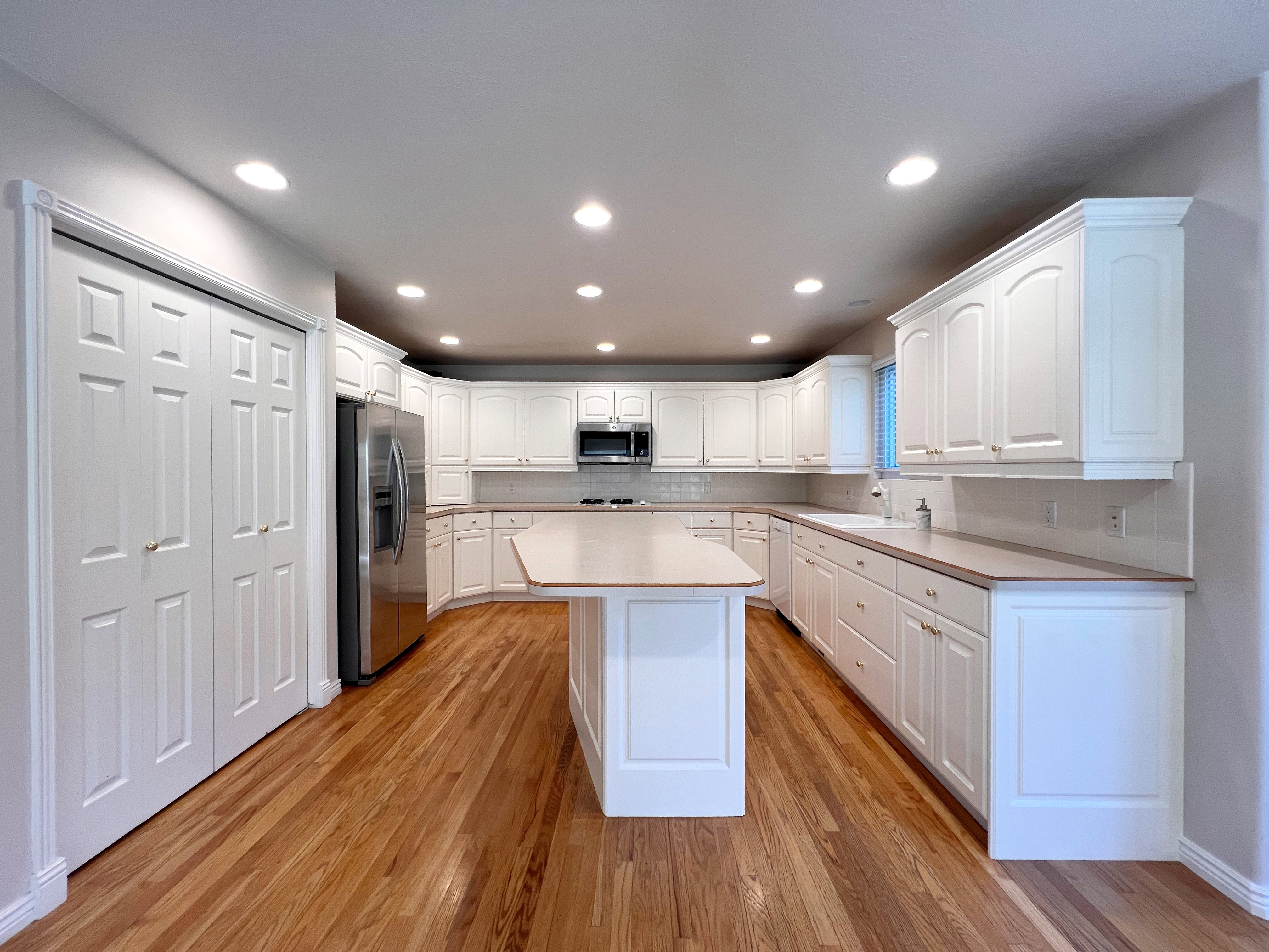 Kitchen featuring extensive white cabinetry, a central island with countertop, wood-finish flooring, a stainless steel refrigerator, and recessed lighting
