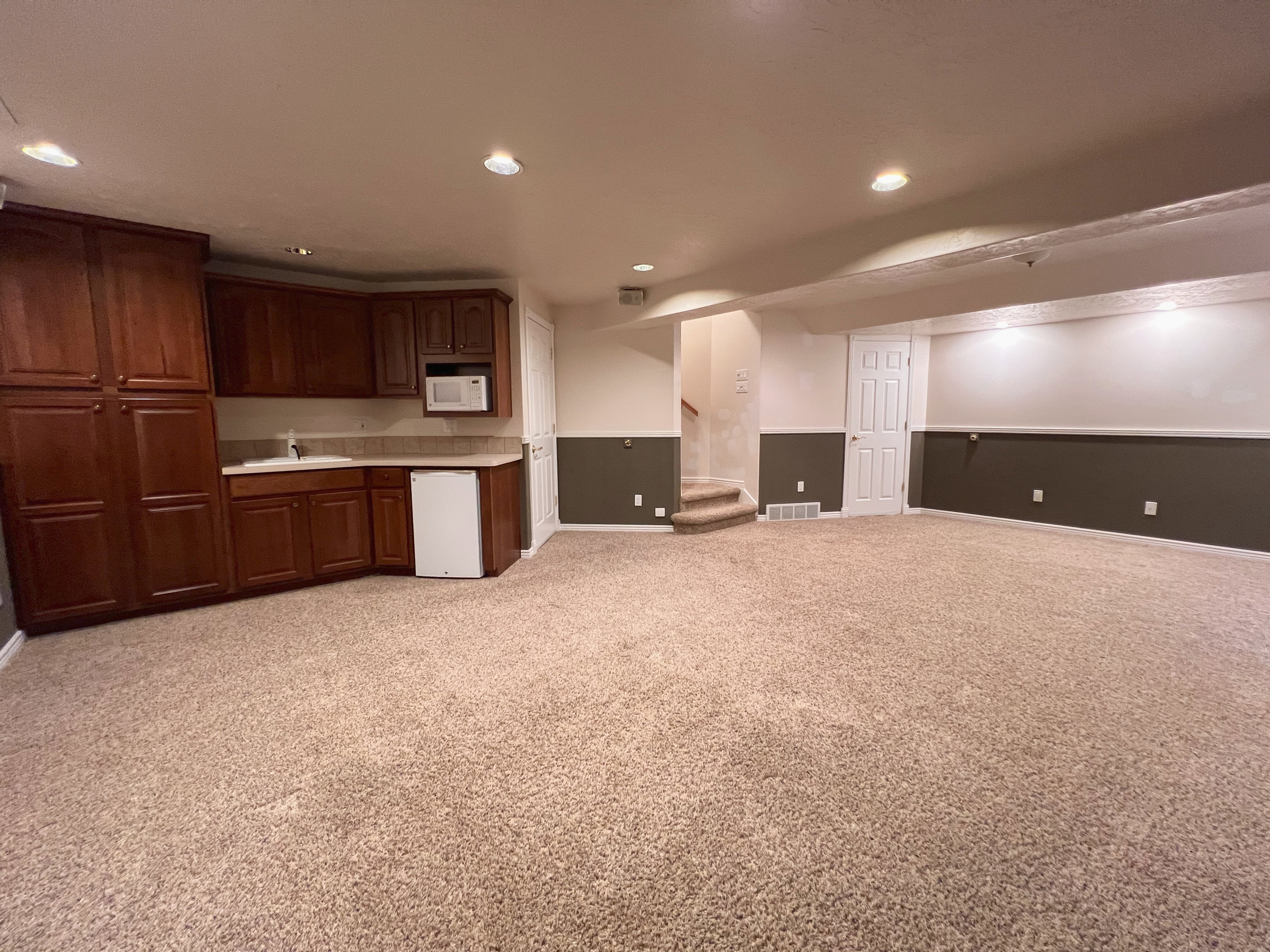 Expansive carpeted area featuring a built-in wet bar with wood cabinetry, a white sink, and a microwave
