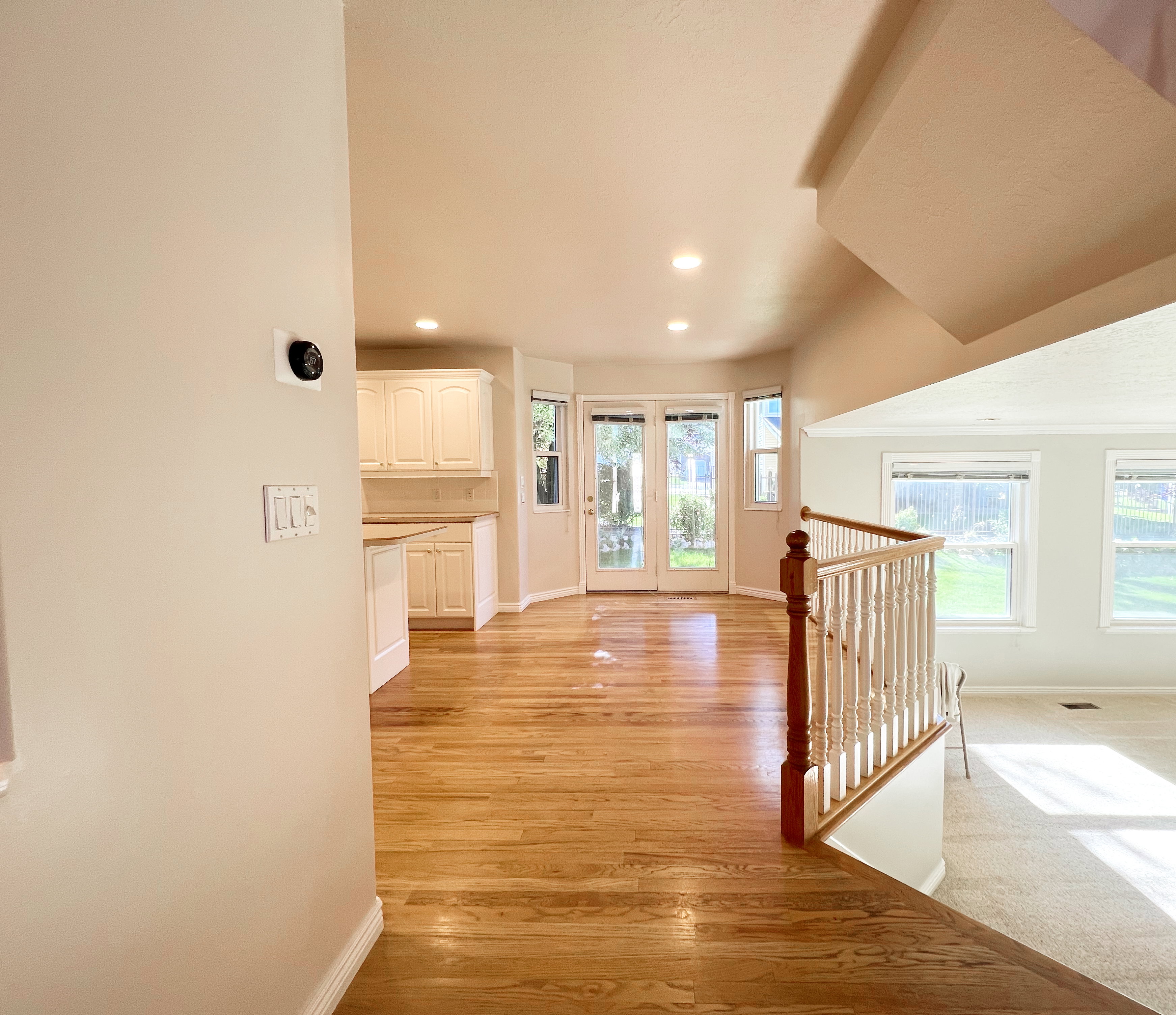 Open-concept living space with wood-finish flooring, white cabinetry, recessed lighting, and a staircase featuring a wood newel post and balusters