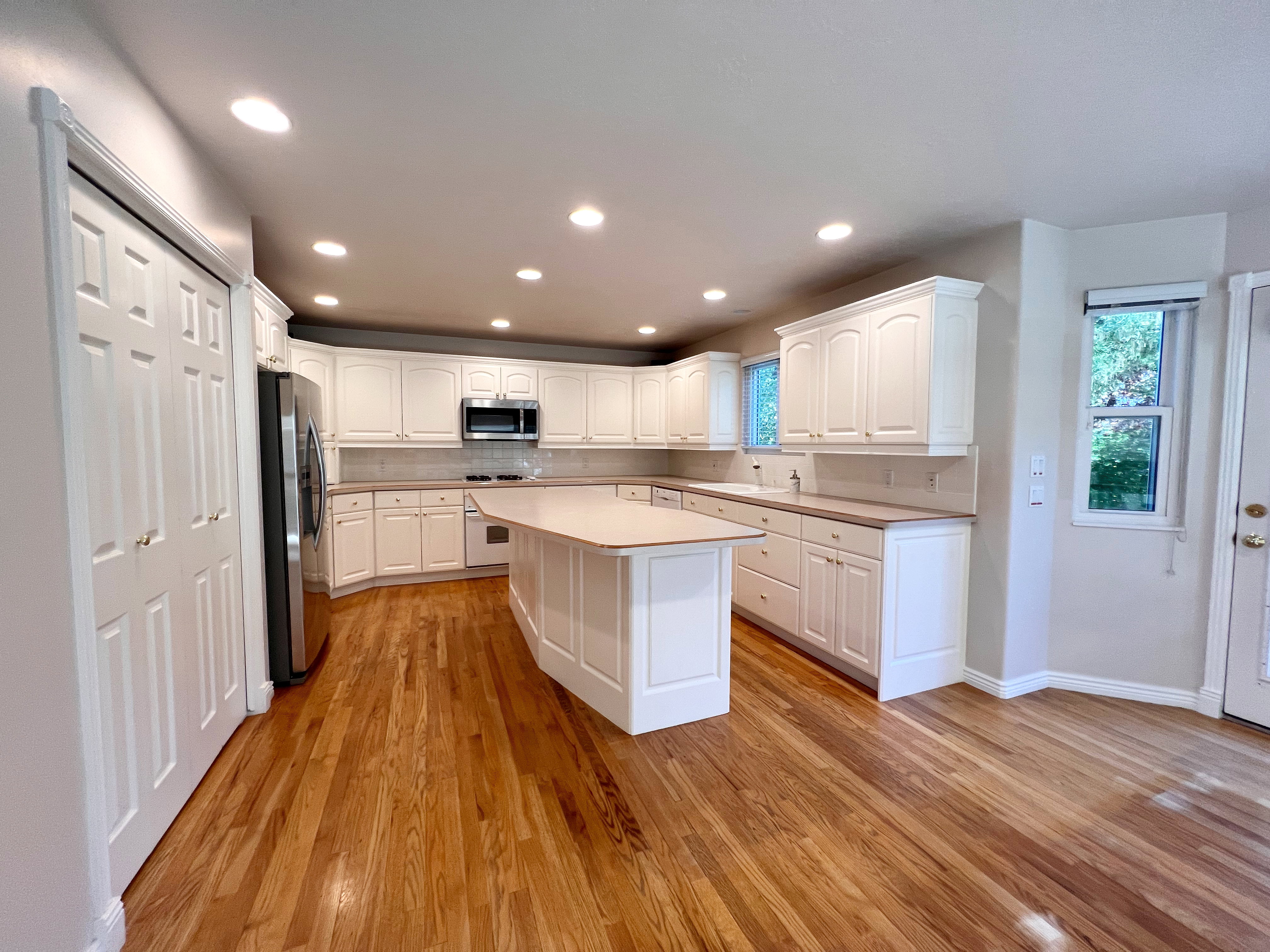 Spacious kitchen featuring an expansive central island, white cabinetry, integrated stainless steel appliances, wood-finish flooring, and recessed lighting