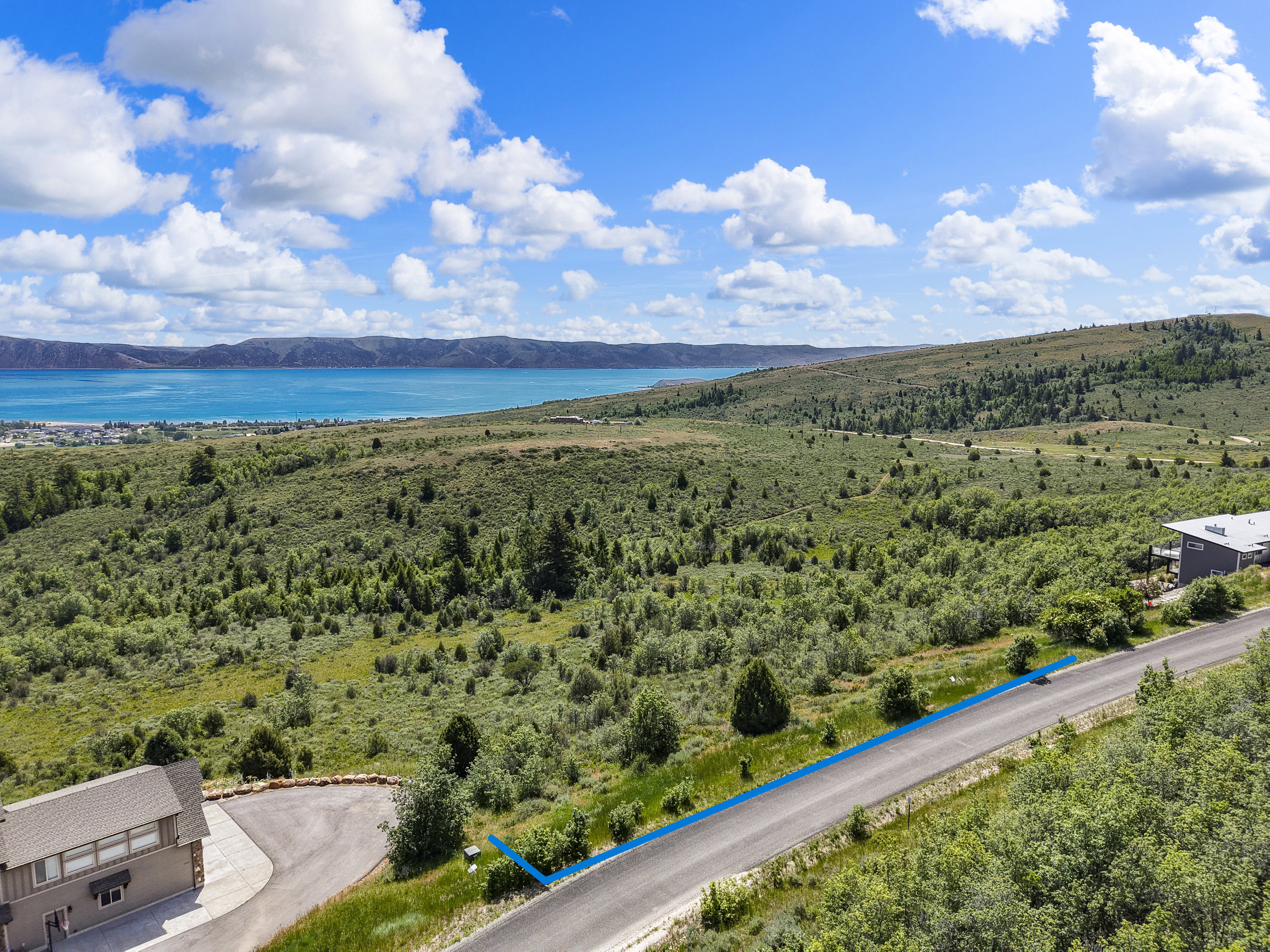 Expansive landscape featuring distant water, a mountainous backdrop, and rolling green hills
