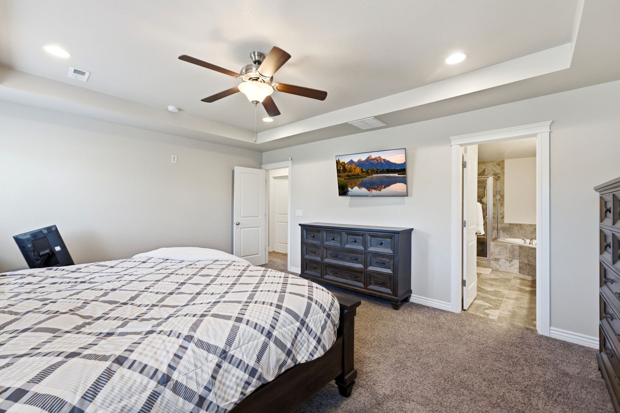 Spacious room featuring tray ceilings with recessed lighting, a ceiling fan, and plush carpeting
