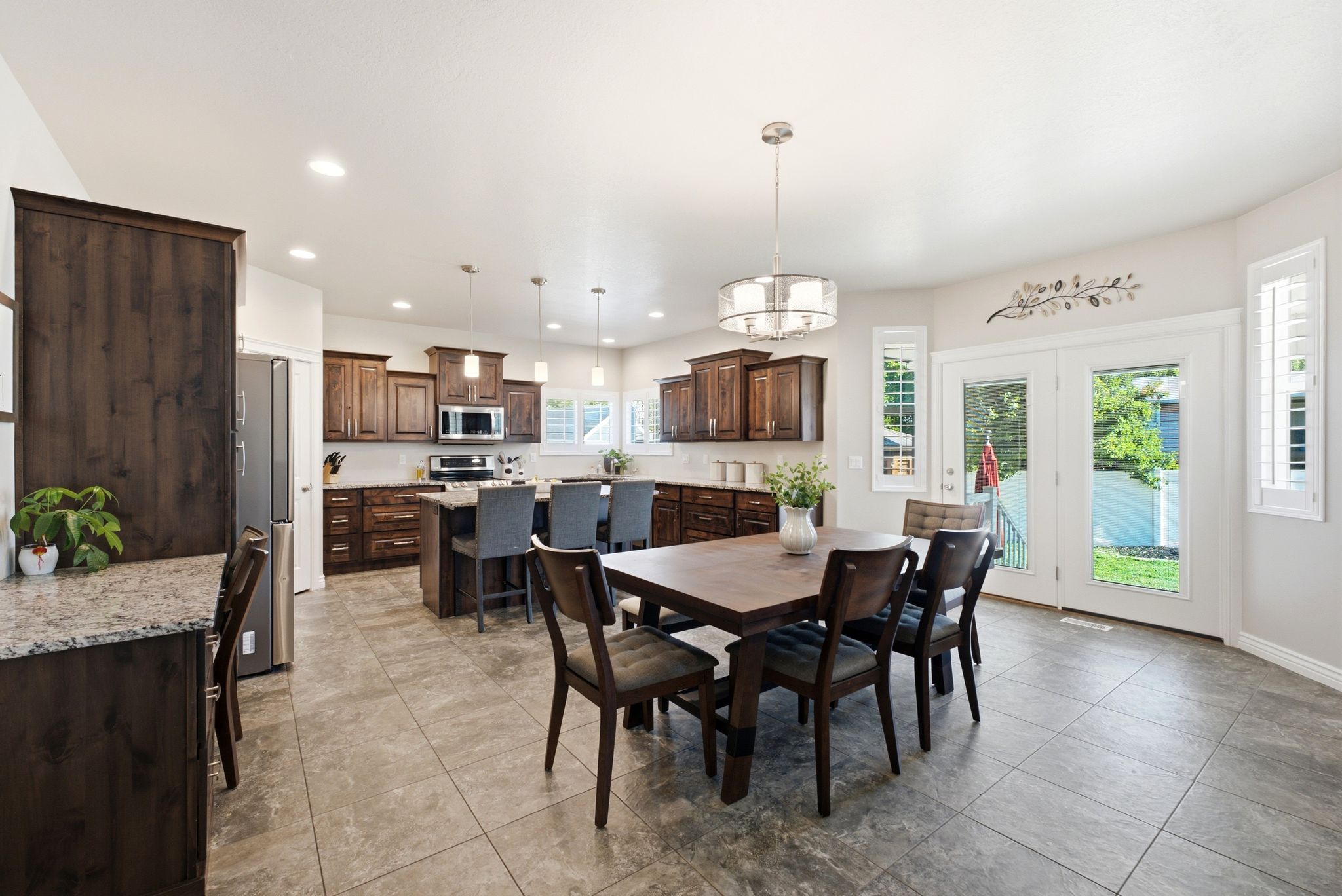 Spacious kitchen and dining area featuring dark wood cabinetry, stainless steel appliances, a large center island with seating, and durable tile flooring