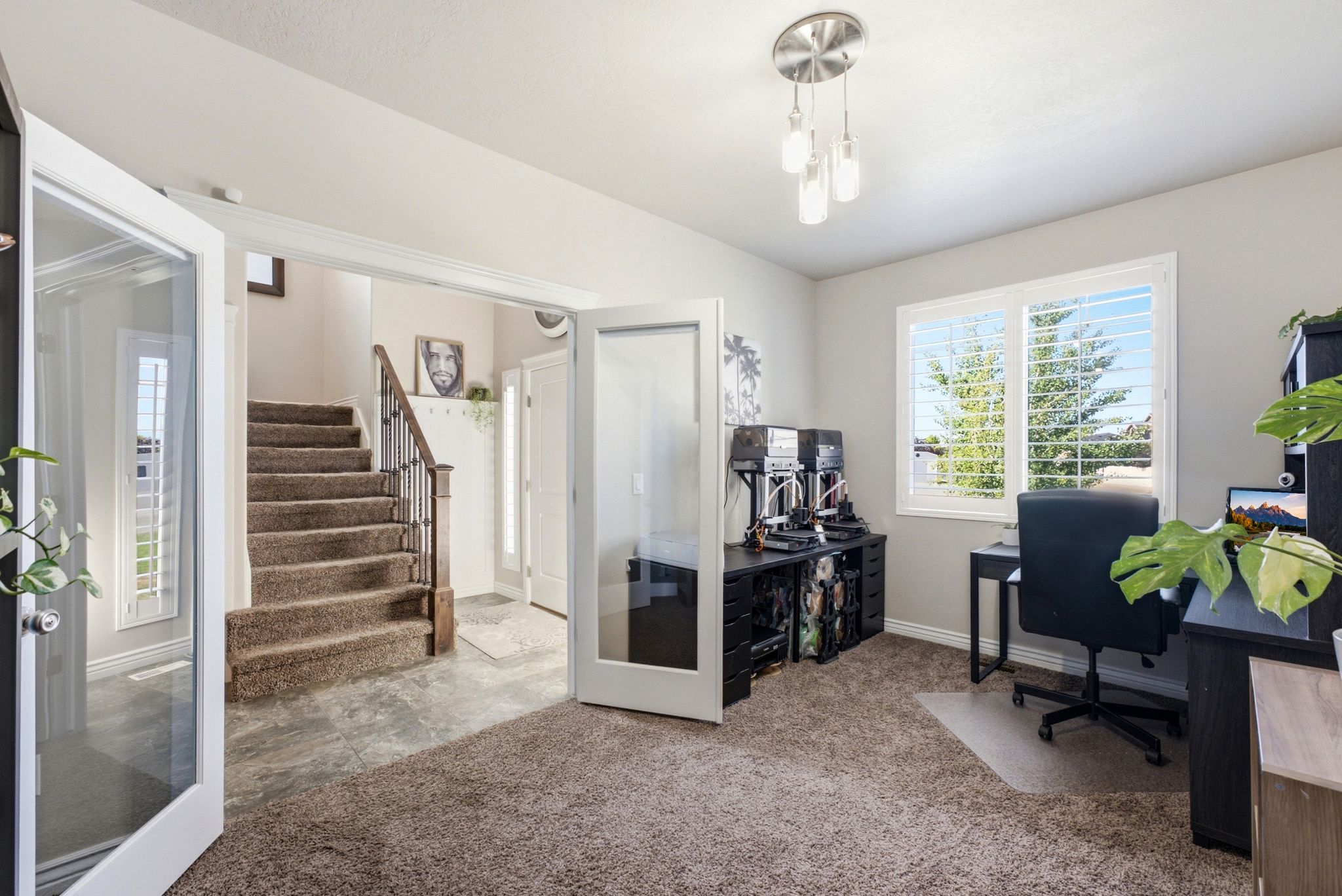 Versatile bonus room with a large window featuring white plantation shutters, brushed nickel pendant light fixture, and neutral carpeting