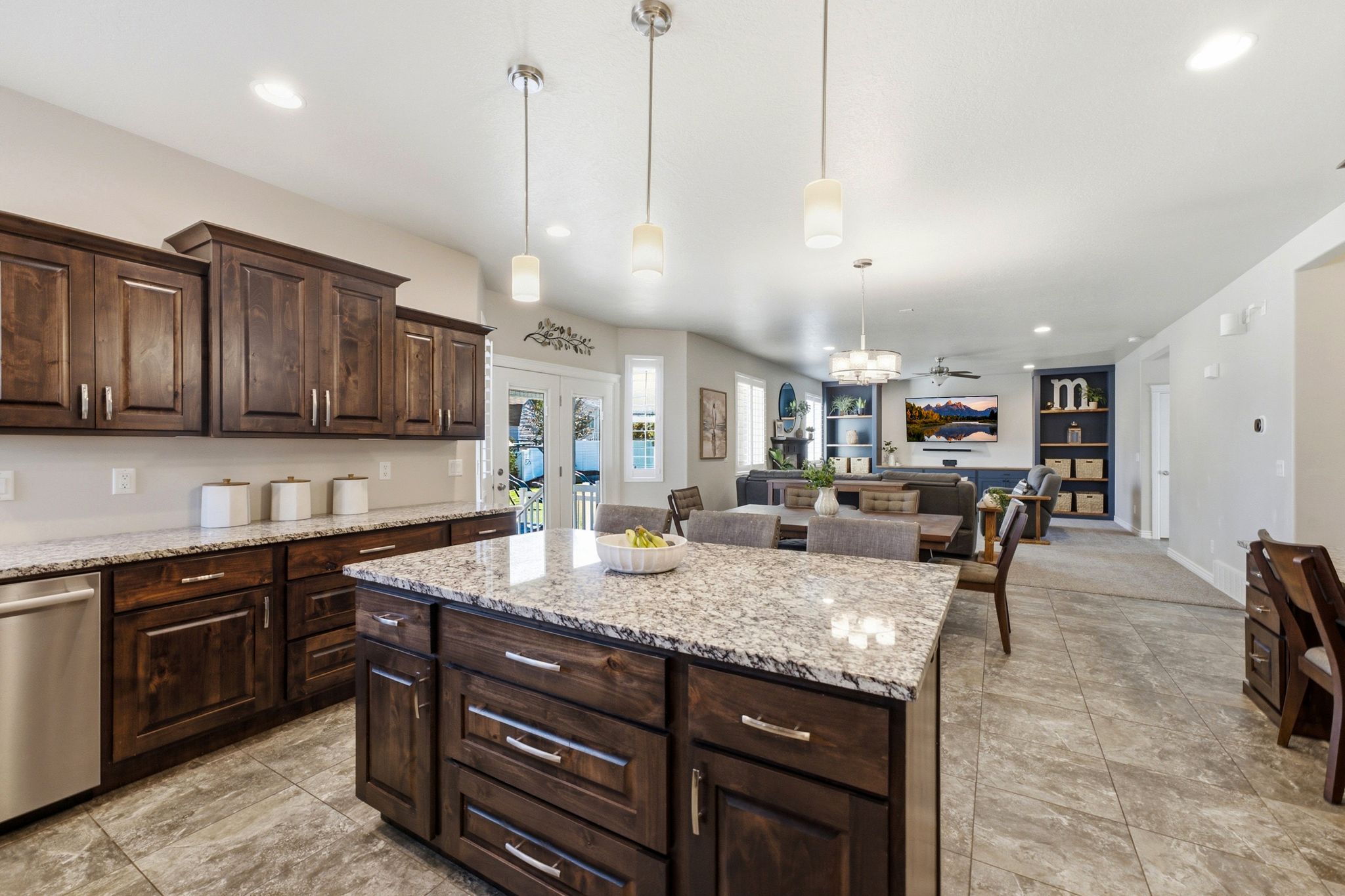 Kitchen featuring a large island with a stone-finish countertop, dark wood cabinetry, stainless steel dishwasher, and tile flooring