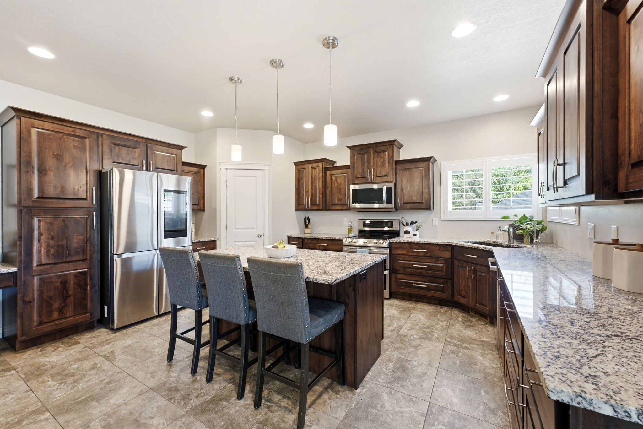 Kitchen featuring an oversized island with seating, stainless steel appliances, dark wood cabinetry, granite countertops, and recessed lighting