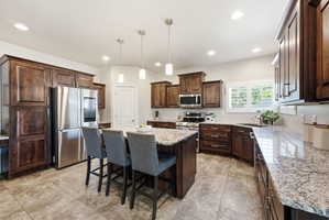 Kitchen featuring an oversized island with seating, stainless steel appliances, dark wood cabinetry, granite countertops, and recessed lighting