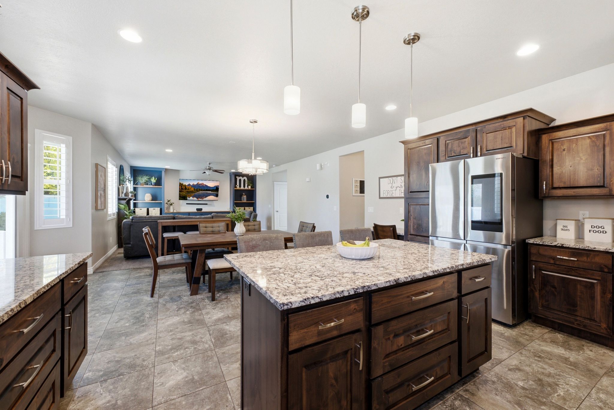 Kitchen featuring a central island with a light-toned countertop, dark wood-finish cabinetry, stainless steel refrigerator, recessed lighting, and pendant lighting fixtures