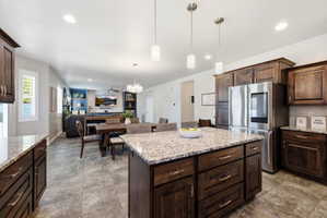 Kitchen featuring a central island with a light-toned countertop, dark wood-finish cabinetry, stainless steel refrigerator, recessed lighting, and pendant lighting fixtures
