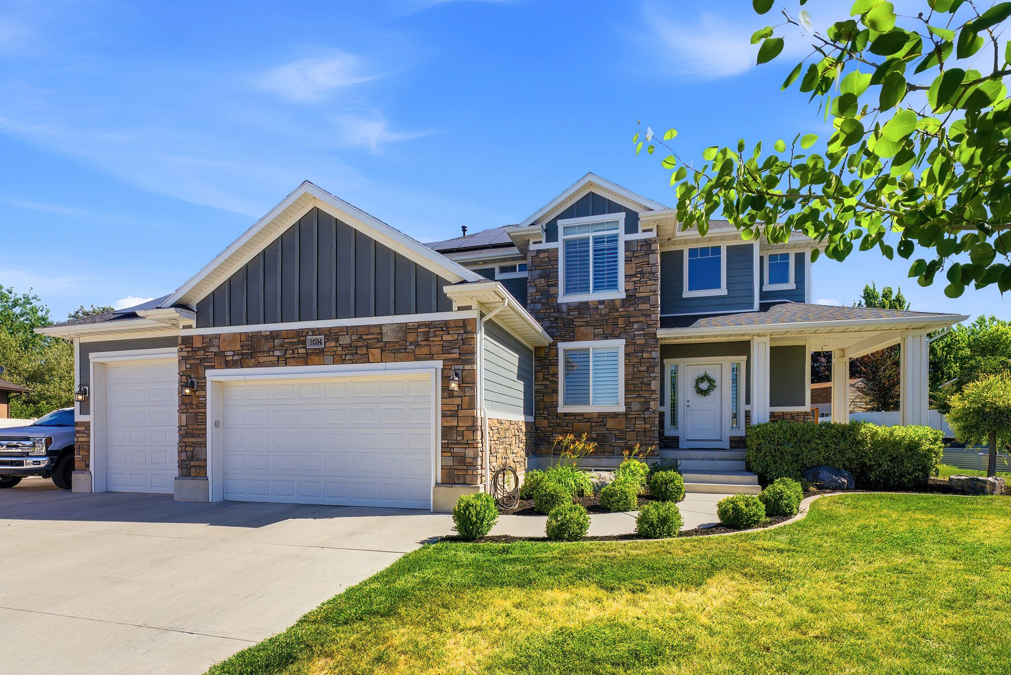 Multi-level residence featuring a stone and siding facade, a covered porch entry, a two-car garage, manicured landscaping, and a concrete driveway