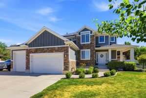 Multi-level residence featuring a stone and siding facade, a covered porch entry, a two-car garage, manicured landscaping, and a concrete driveway