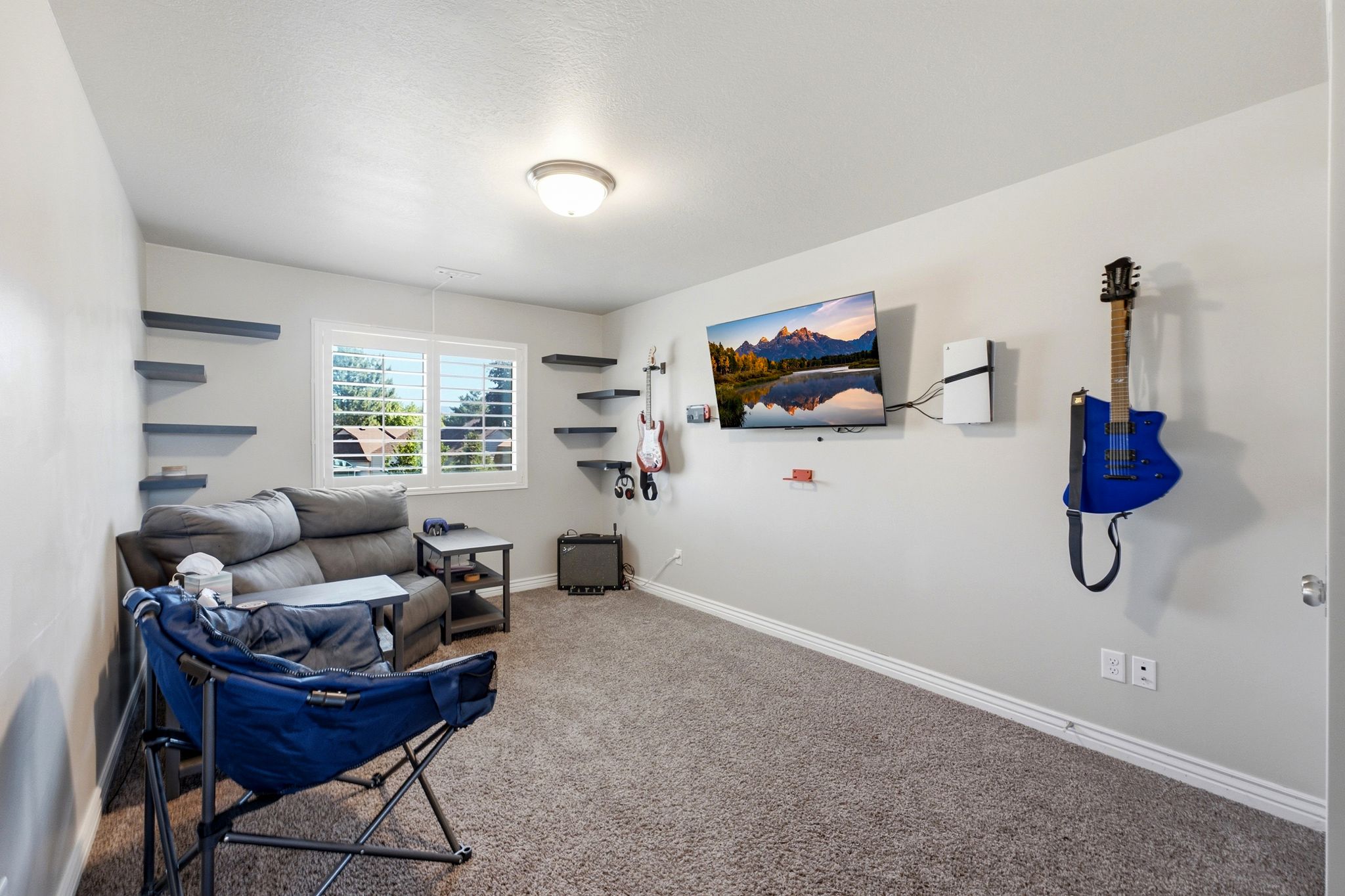 Carpeted room featuring built-in wall shelving, a window with plantation shutters, baseboard molding, and a flush-mount ceiling light fixture