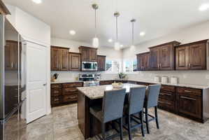 Kitchen featuring a large central island with seating, dark wood-finish cabinetry, light-toned countertops, and recessed lighting