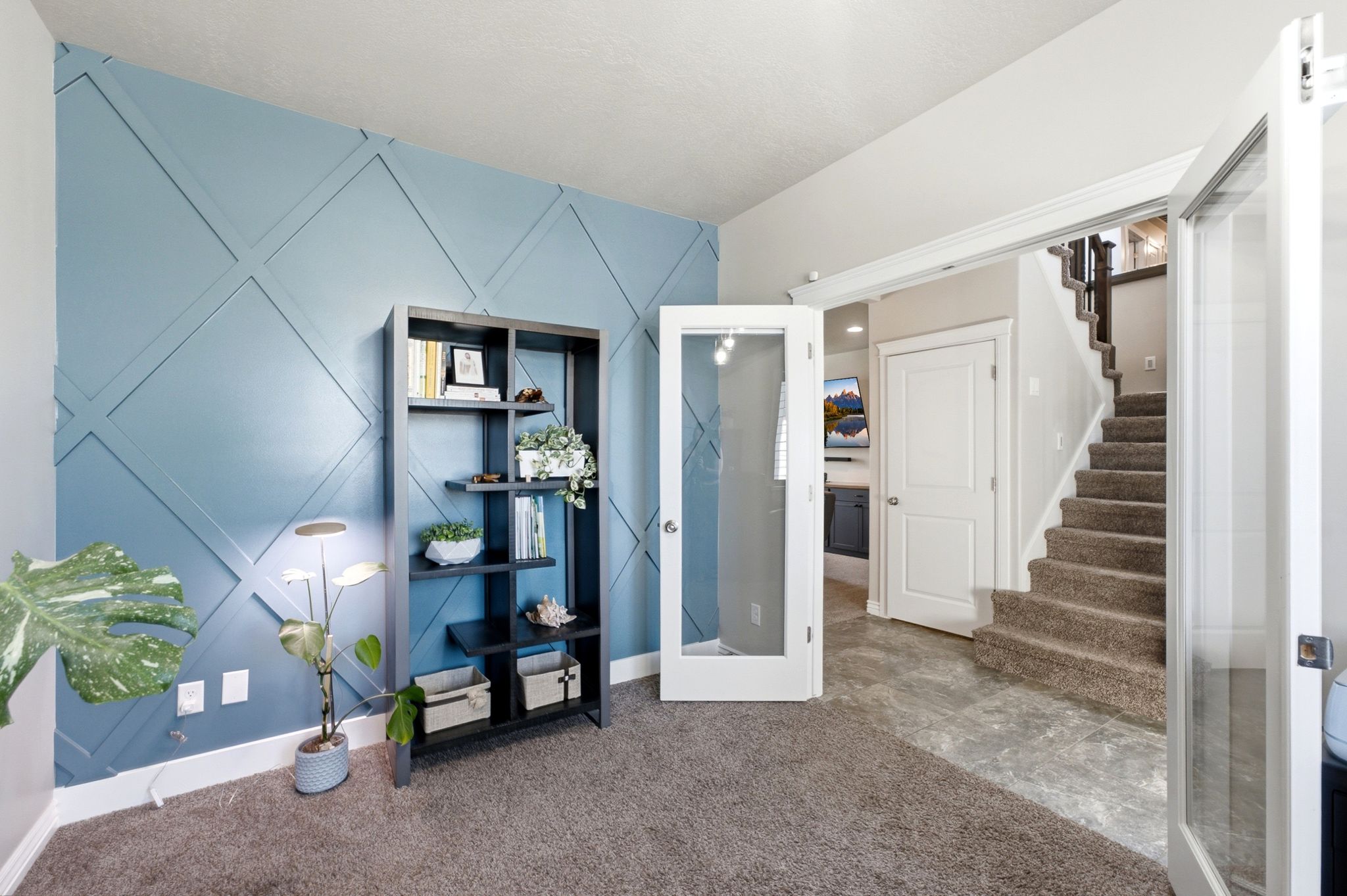 Room featuring a decorative accent wall with geometric paneling, carpeted flooring, and French doors