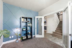 Room featuring a decorative accent wall with geometric paneling, carpeted flooring, and French doors