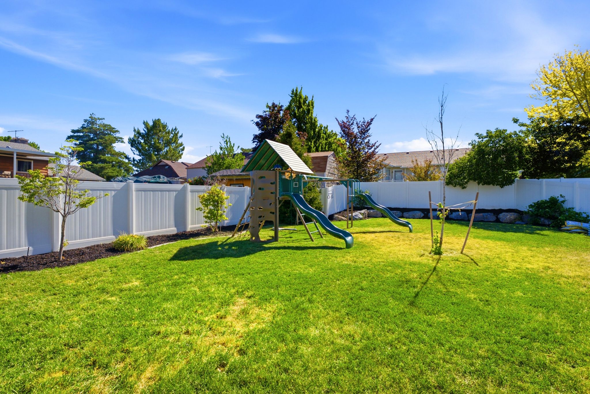Spacious backyard featuring a lush lawn, white vinyl fencing, and mature trees