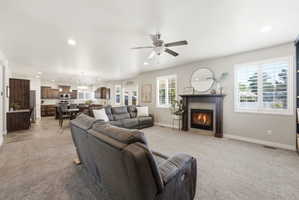 Open-concept living space featuring a fireplace with a dark wood mantel and tile surround, recessed lighting, ceiling fan, and multiple windows with plantation shutters