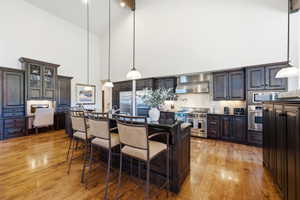 Vaulted ceilings enhance this kitchen featuring hardwood flooring, dark wood cabinetry, a central island with bar seating, and stainless steel appliances