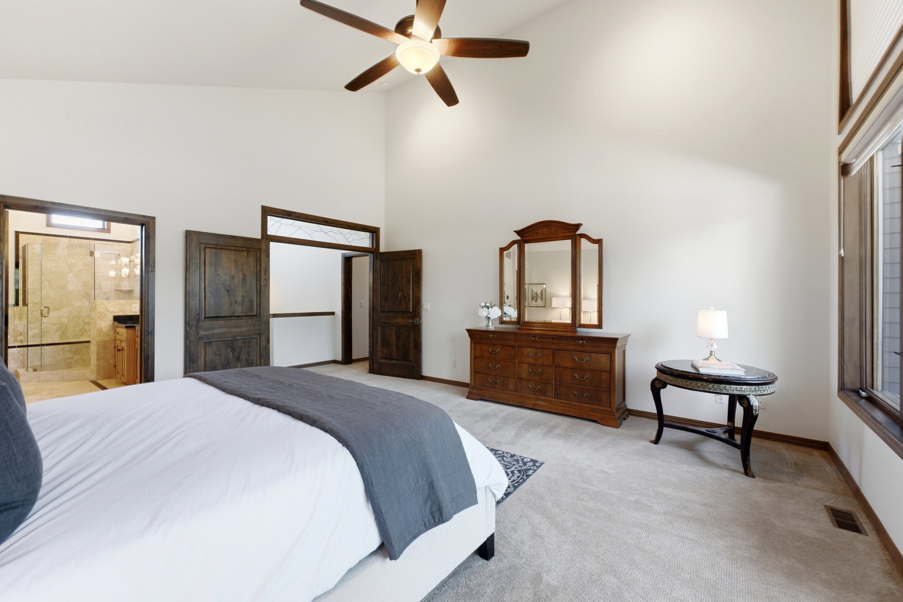 Vaulted ceiling with a ceiling fan, carpet flooring, large windows, and a bathroom entrance featuring a glass-enclosed shower