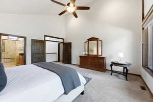 Vaulted ceiling with a ceiling fan, carpet flooring, large windows, and a bathroom entrance featuring a glass-enclosed shower